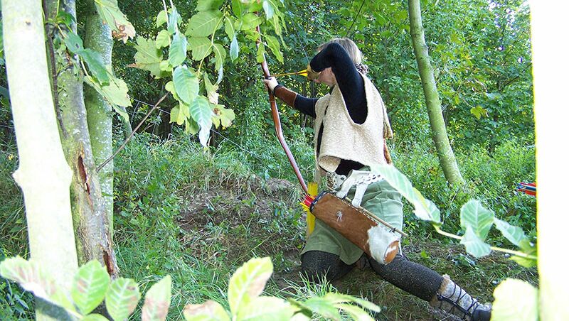 TeamBuilding - Intuitives Bogenschießen - Frau im Wald mit Pfeil und Bogen